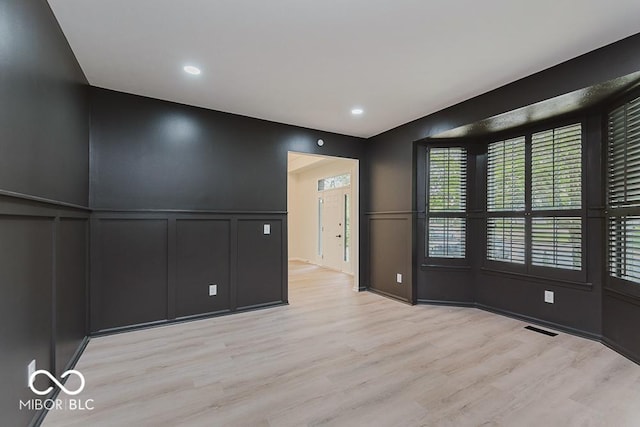 empty room featuring a decorative wall, light wood-type flooring, wainscoting, and recessed lighting
