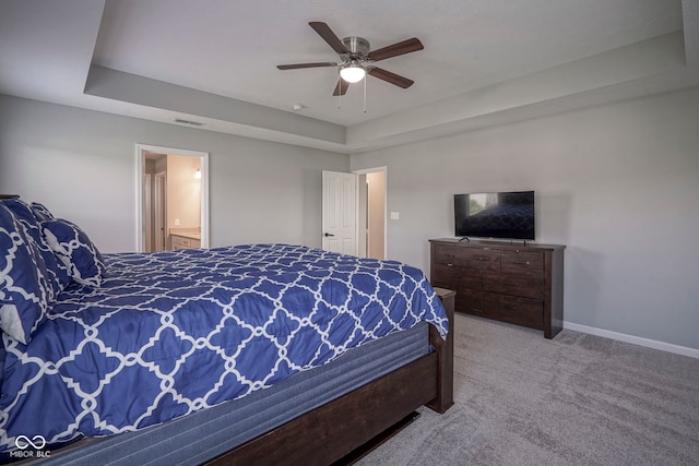 bedroom featuring carpet floors, baseboards, ceiling fan, a tray ceiling, and ensuite bath