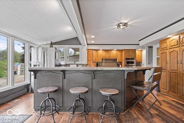 kitchen with stainless steel appliances, a breakfast bar area, wood finished floors, a baseboard radiator, and lofted ceiling