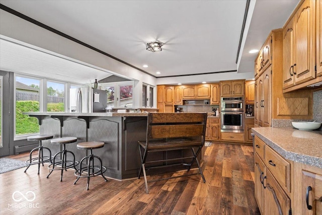 kitchen featuring stainless steel appliances, a kitchen breakfast bar, dark wood-style floors, backsplash, and recessed lighting