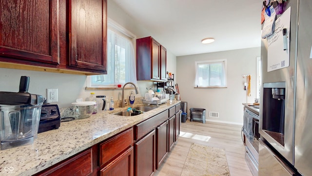 kitchen featuring stainless steel refrigerator with ice dispenser, a sink, light wood-style floors, dark brown cabinets, and light stone countertops