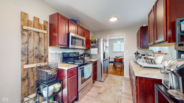 kitchen with stainless steel appliances, reddish brown cabinets, light wood-style floors, and light stone counters