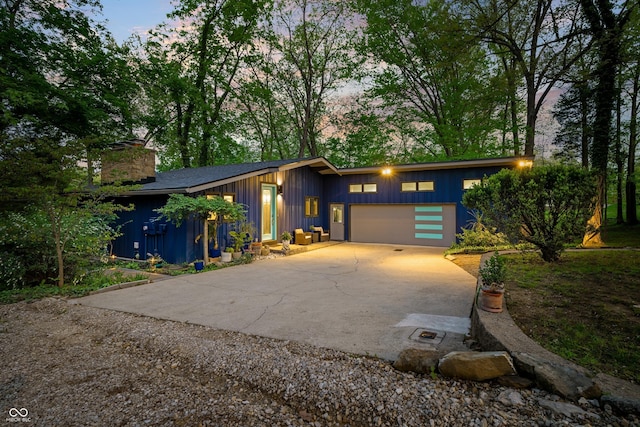 7753 Ivy Dr, Nineveh, IN 46164 - mid-century modern home featuring concrete driveway, an attached garage, board and batten siding, and a chimney
