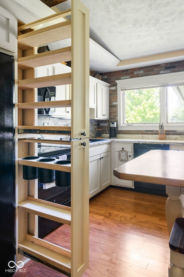 kitchen featuring dishwashing machine, a textured ceiling, white cabinetry, light wood-type flooring, and light countertops
