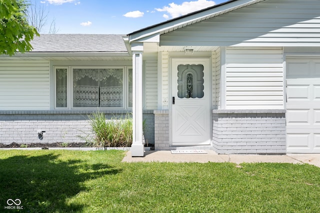 doorway to property with brick siding, a lawn, a garage, and a shingled roof