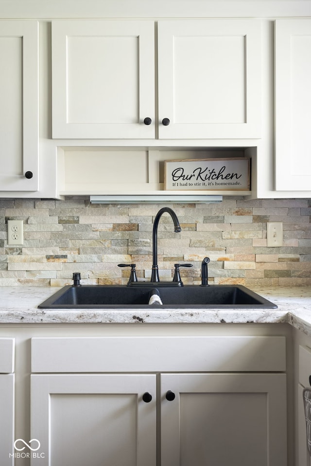 kitchen view of a sink, tasteful backsplash, white cabinetry, and light stone countertops