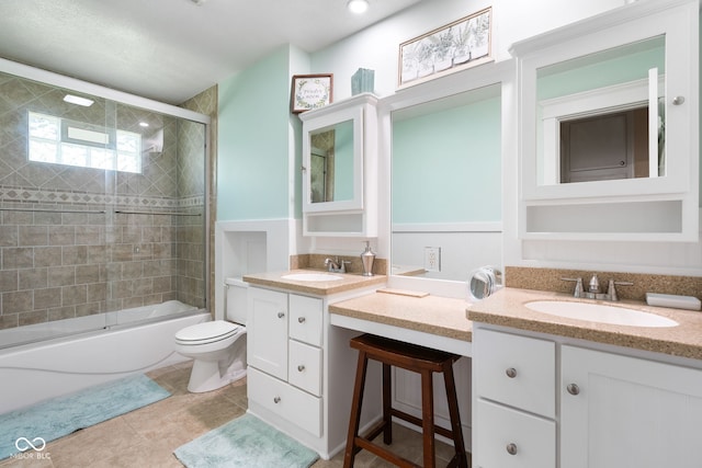 bathroom featuring two vanities, combined bath / shower with glass door, toilet, and tile patterned flooring