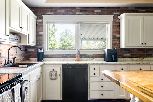 kitchen featuring black dishwasher, a sink, butcher block countertops, white cabinets, and brick wall