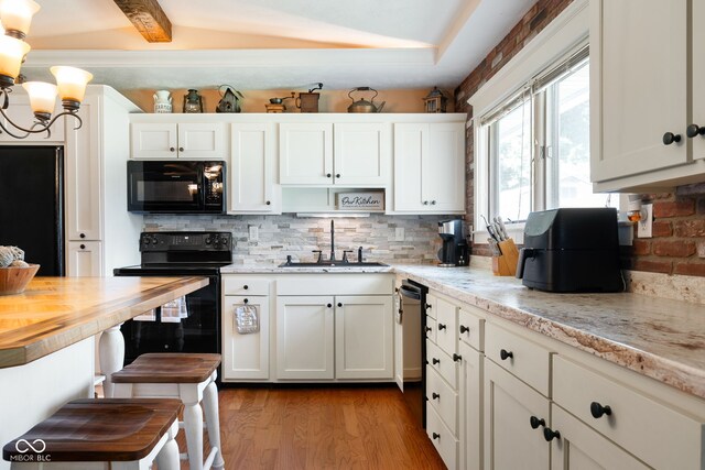 kitchen with black appliances, a sink, decorative backsplash, light wood-style flooring, and white cabinets