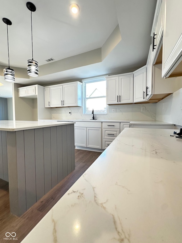 337 N Beville Ave, Indianapolis, IN 46201 - kitchen with dark wood finished floors, light stone countertops, white cabinetry, and decorative light fixtures