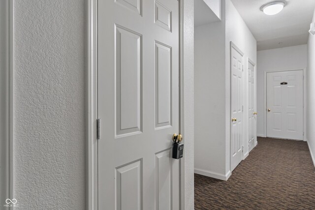 corridor featuring dark colored carpet and baseboards