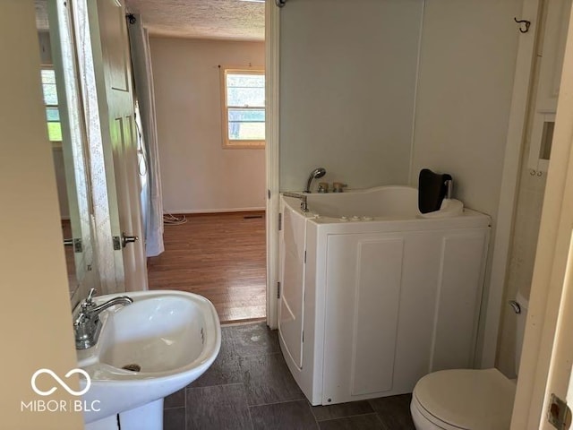 bathroom with a sink, toilet, a textured ceiling, a tub, and wood finished floors