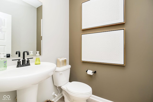 bathroom with baseboards, toilet, and a sink