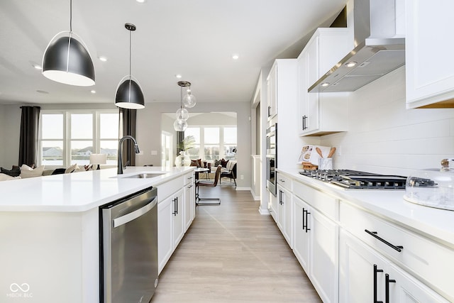 kitchen featuring stainless steel appliances, a sink, wall chimney range hood, open floor plan, and backsplash