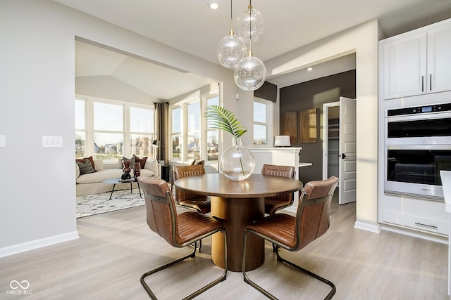 dining room featuring light wood-style floors, plenty of natural light, baseboards, and vaulted ceiling