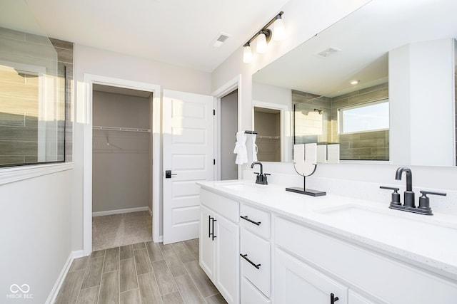 bathroom with a shower stall, a spacious closet, double vanity, wood finished floors, and baseboards