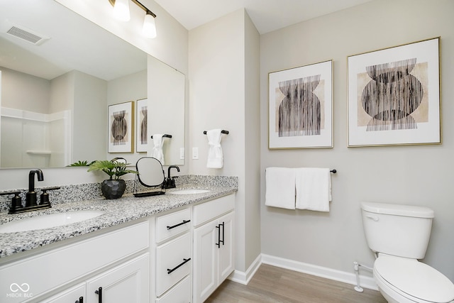 bathroom with baseboards, wood finished floors, toilet, and double vanity