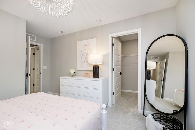 bedroom featuring light carpet, a walk in closet, a closet, a chandelier, and baseboards