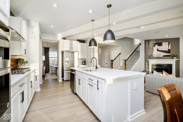 kitchen with a sink, appliances with stainless steel finishes, light wood-style flooring, light countertops, and open floor plan