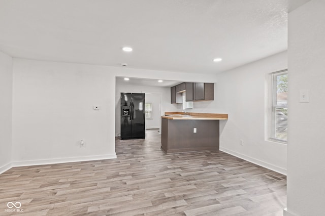 2321 W 26th St, Anderson, IN 46016 - kitchen with black fridge, light wood finished floors, a peninsula, light countertops, and baseboards