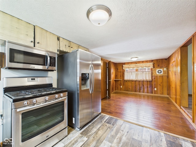 kitchen featuring stainless steel appliances, light wood-style floors, a textured ceiling, wood walls, and baseboards