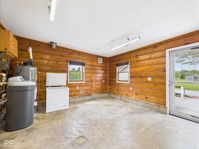 unfurnished living room featuring plenty of natural light, water heater, unfinished concrete floors, and wooden walls
