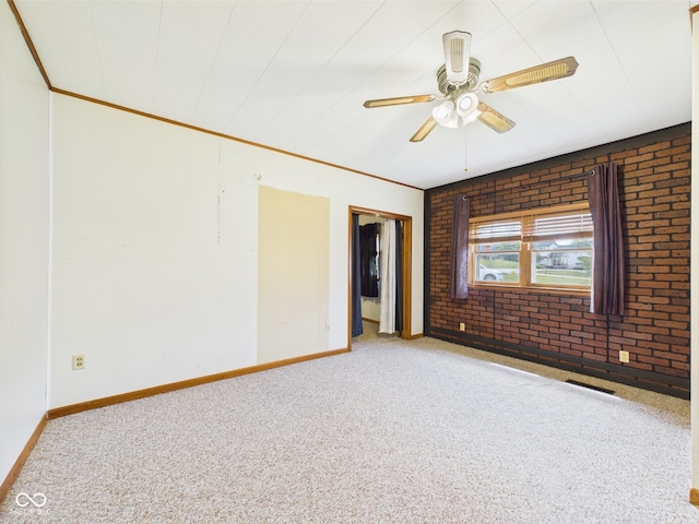 carpeted spare room featuring baseboards, ceiling fan, brick wall, and crown molding
