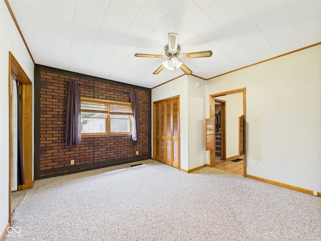 unfurnished bedroom featuring carpet flooring, a closet, ornamental molding, brick wall, and ceiling fan