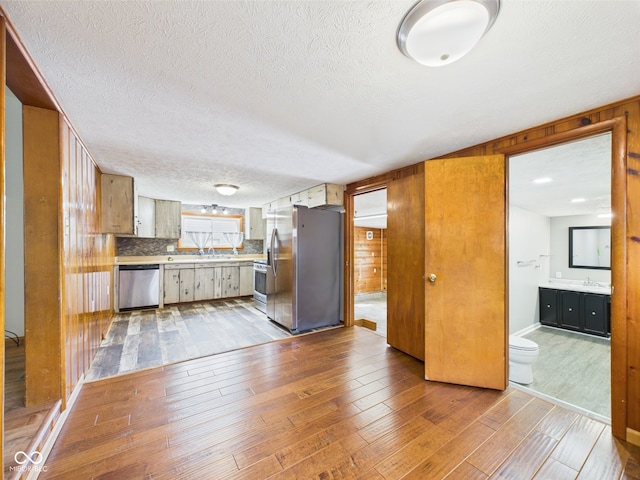 kitchen featuring stainless steel appliances, hardwood / wood-style floors, wood walls, a textured ceiling, and light countertops