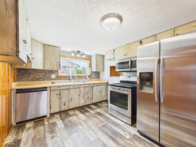 kitchen featuring stainless steel appliances, a sink, wood finished floors, backsplash, and a textured ceiling