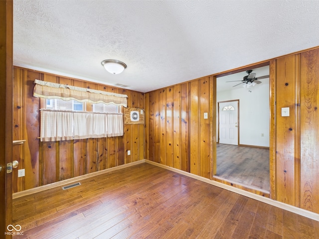 empty room featuring wood-type flooring, a textured ceiling, baseboards, ceiling fan, and wooden walls