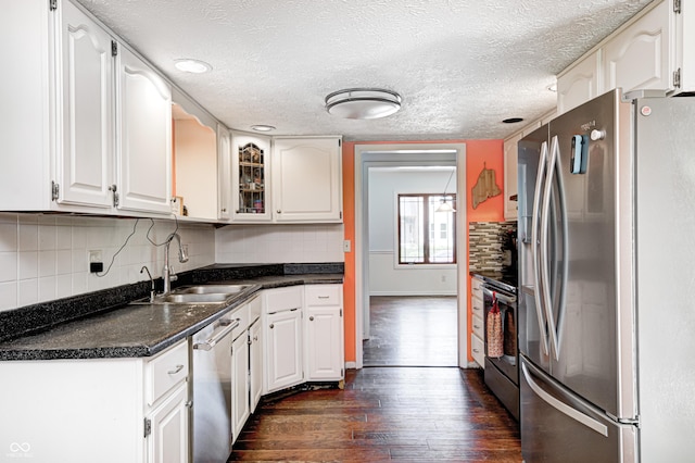 kitchen featuring stainless steel appliances, dark wood-style floors, a sink, dark countertops, and white cabinets