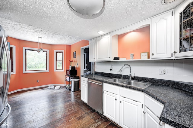 kitchen with appliances with stainless steel finishes, a sink, dark countertops, a textured ceiling, and dark wood-style flooring