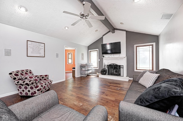 living area featuring wood-type flooring, a textured ceiling, ceiling fan, a large fireplace, and baseboards