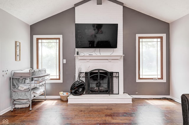 living area featuring a brick fireplace, vaulted ceiling, wood-type flooring, and baseboards