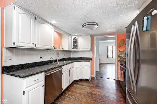 kitchen with appliances with stainless steel finishes, a sink, dark wood-style floors, white cabinetry, and a textured ceiling