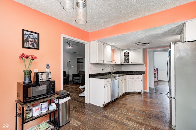 kitchen with stainless steel appliances, a textured ceiling, a sink, white cabinets, and dark wood-style flooring