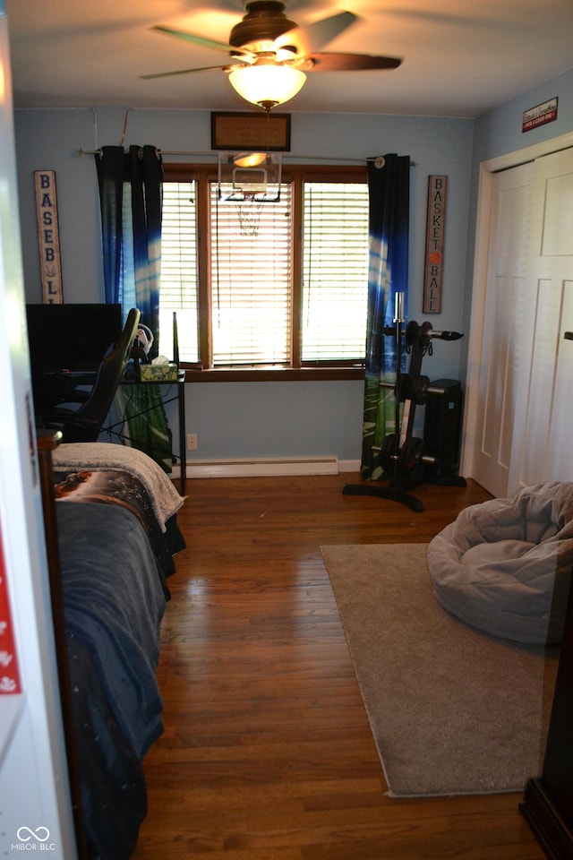 bedroom with wood finished floors, baseboard heating, baseboards, a ceiling fan, and a closet