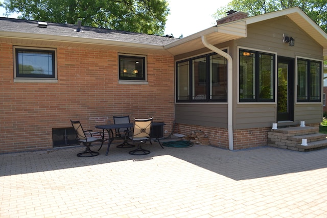 back of house with a patio area, a sunroom, a chimney, and brick siding