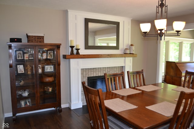 dining space featuring dark wood-style flooring, a tile fireplace, a chandelier, and baseboards