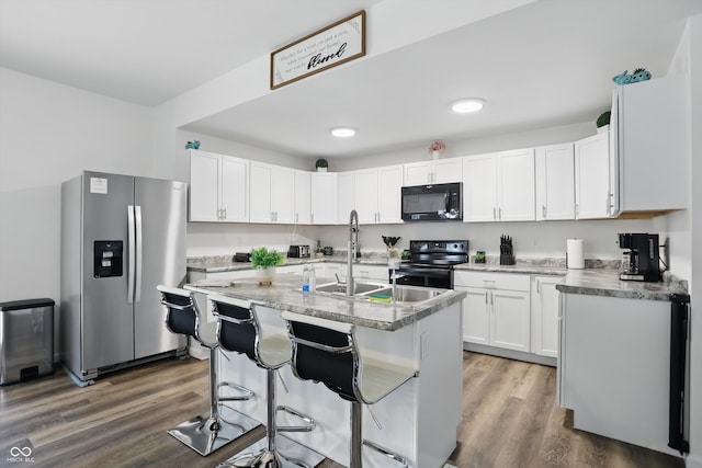 kitchen featuring appliances with stainless steel finishes, wood finished floors, white cabinetry, an island with sink, and a breakfast bar area