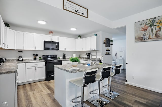 kitchen featuring black appliances, a sink, wood finished floors, white cabinetry, and recessed lighting