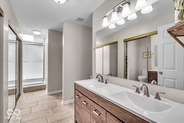 bathroom with toilet, double vanity, an enclosed shower, and baseboards
