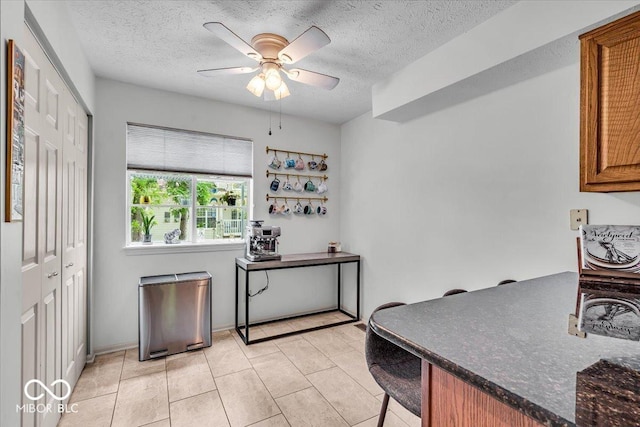 kitchen featuring a ceiling fan, a textured ceiling, brown cabinets, light tile patterned floors, and a kitchen bar