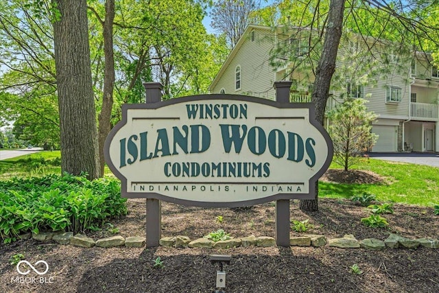 community sign featuring asphalt driveway and a garage