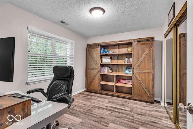 office featuring light wood finished floors, a barn door, a textured ceiling, and baseboards