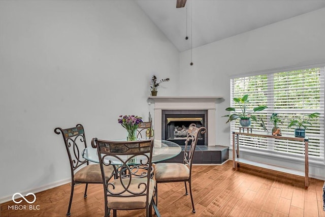 dining area with a fireplace, wood finished floors, high vaulted ceiling, baseboards, and ceiling fan