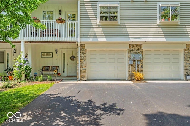 view of front of house with stone siding, a garage, driveway, and a balcony