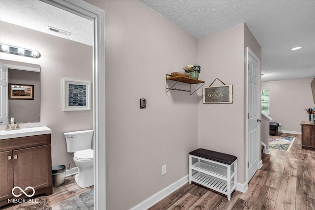 bathroom with a textured ceiling, wood finished floors, toilet, vanity, and baseboards