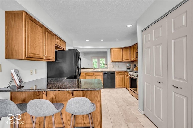 kitchen with black appliances, a sink, brown cabinetry, a peninsula, and recessed lighting